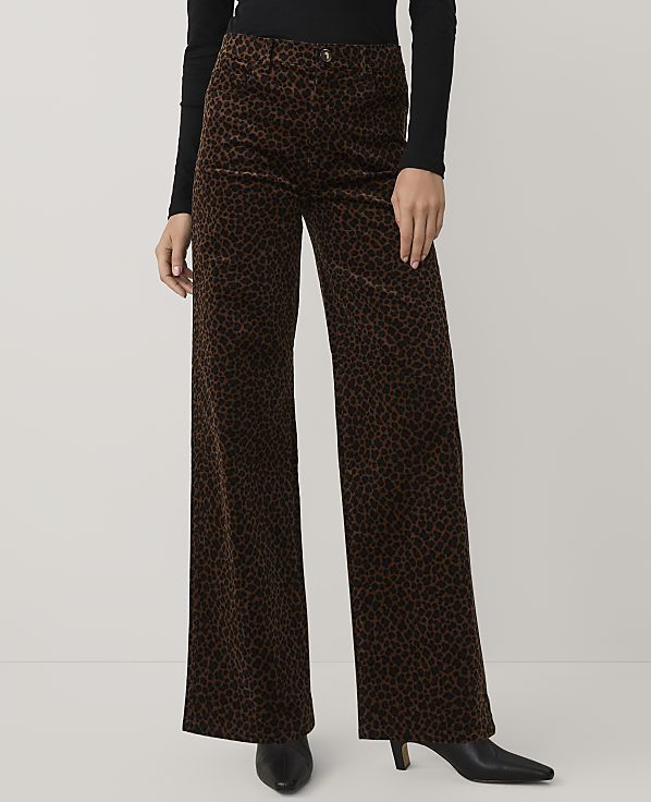 A person wearing a black top and brown leopard-print wide-leg trousers stands against a plain light gray background.