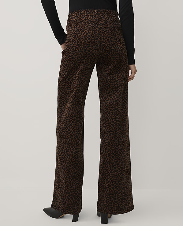 A person wearing a black top and brown leopard-print wide-leg trousers stands against a plain light gray background.