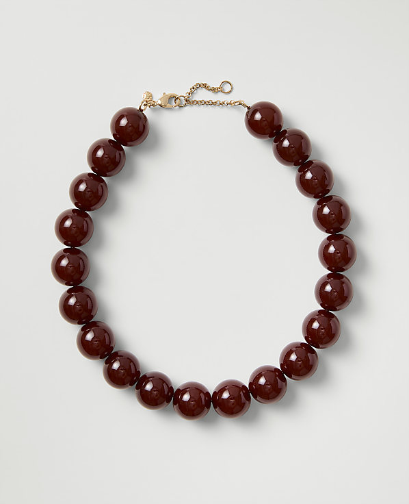 A necklace of polished deep red beads with a gold clasp rests on a plain light gray background.