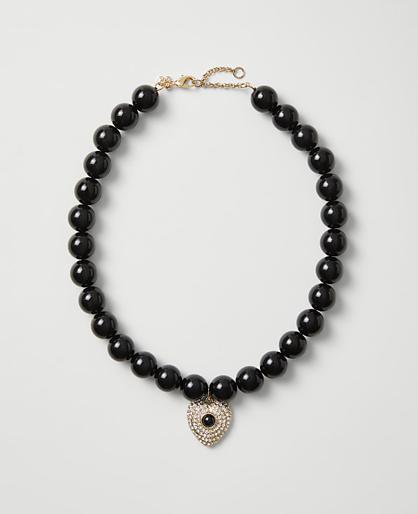 A necklace of polished black beads with a heart-shaped crystal pendant rests on a plain light gray background.