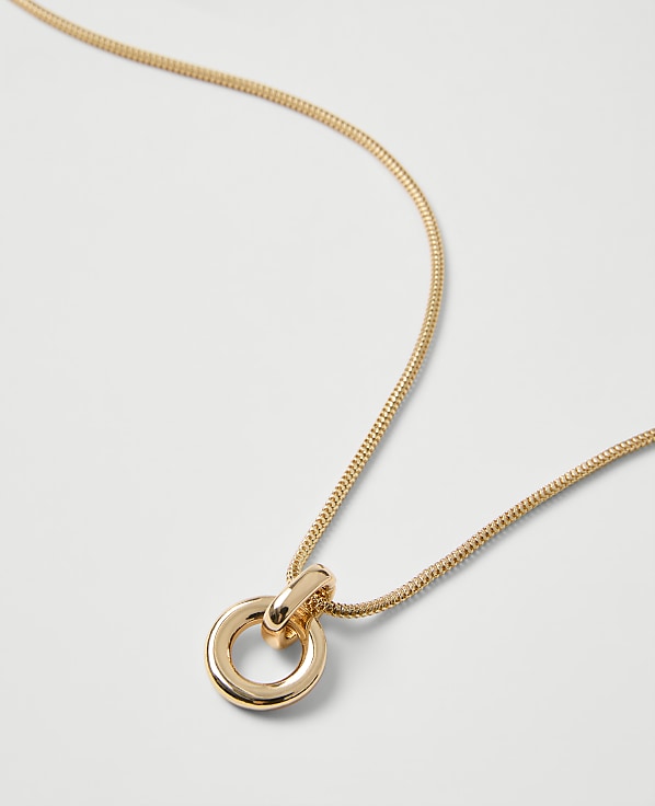 A gold snake chain necklace with a circular pendant rests on a plain white background.