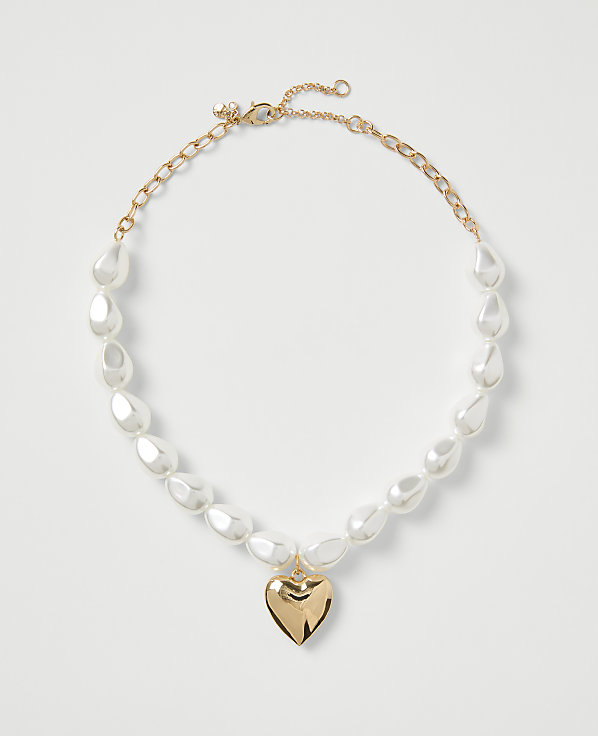 A gold-toned necklace with white teardrop pearls and a heart pendant rests on a plain white background.