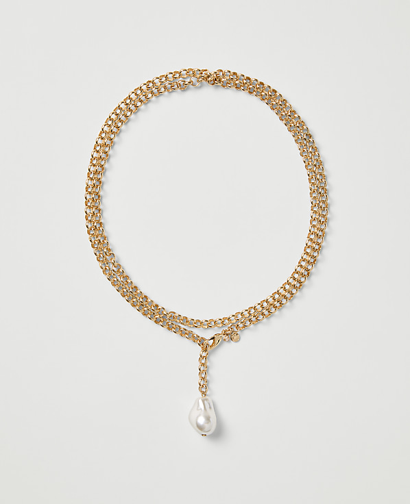 A gold chain necklace with a single white pearl drop pendant rests on a plain light gray background.