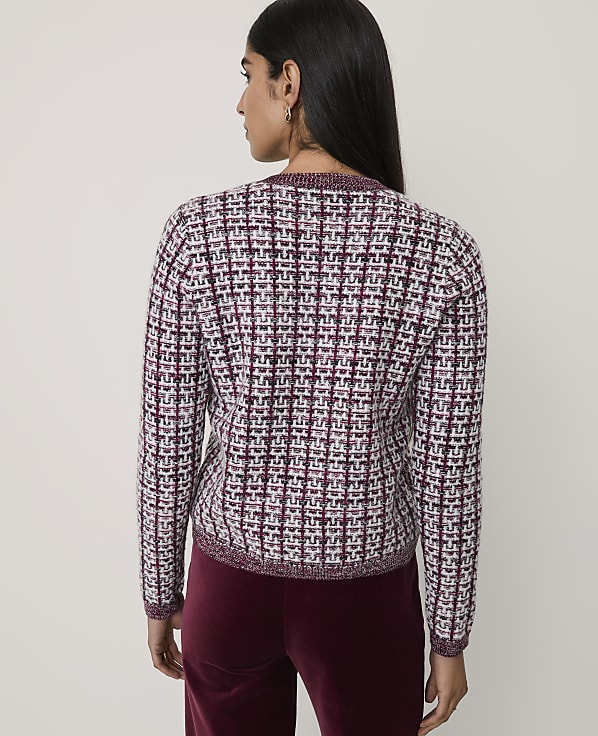 A woman stands with her back to the camera wearing a textured maroon and white tweed jacket and maroon velvet trousers against a plain light grey background.