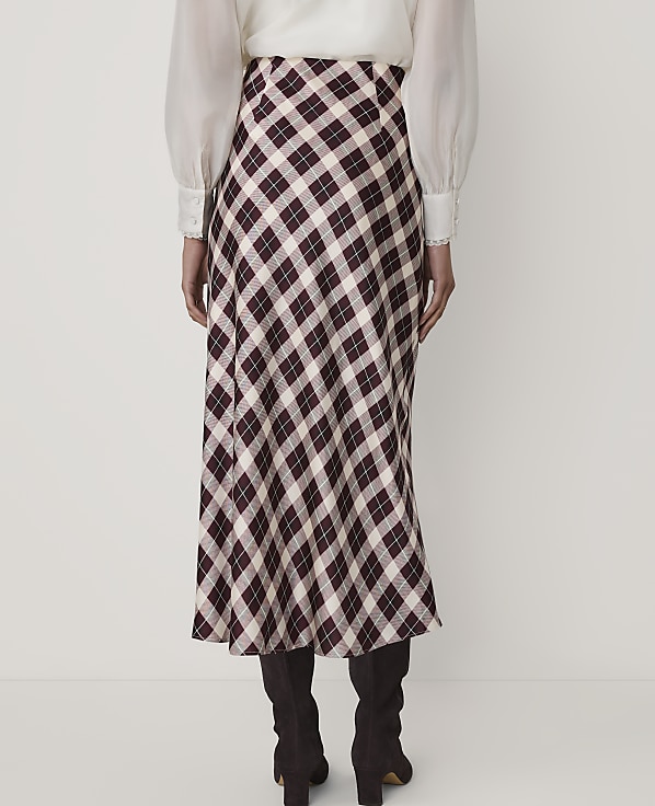 A person wearing a white blouse, a plaid midi skirt, and dark boots stands against a plain white background.