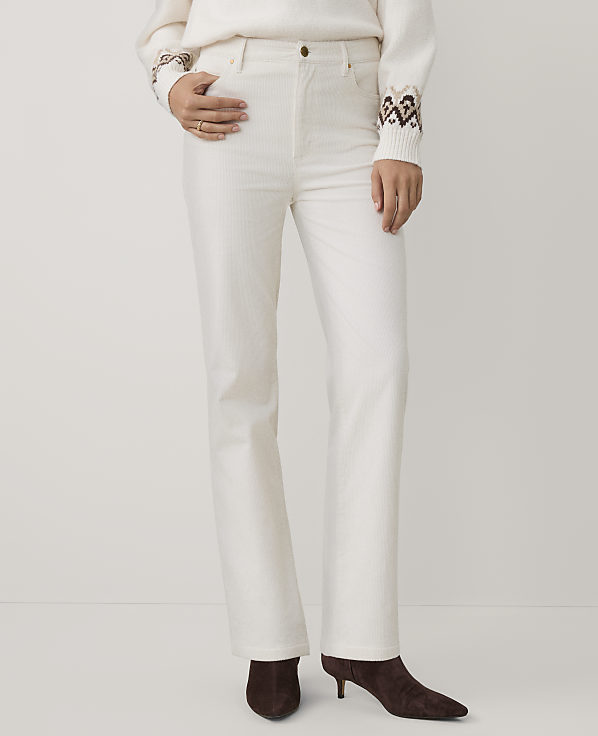 A person wearing a white sweater and white trousers with brown boots stands against a plain white background.
