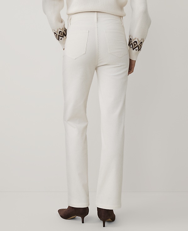A person wearing a white sweater and white trousers with brown heels stands against a plain white background.