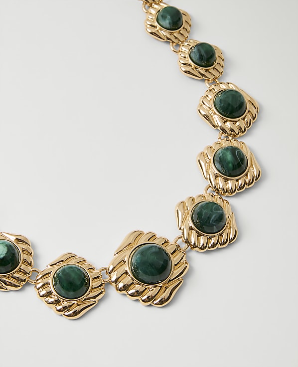 A gold necklace with green malachite stones rests against a plain white background.