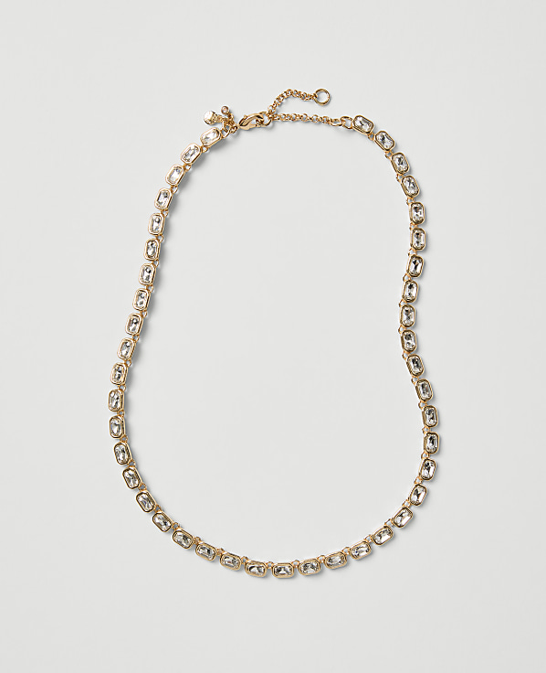 A gold-toned necklace with clear crystals is laid out against a plain, light gray background.