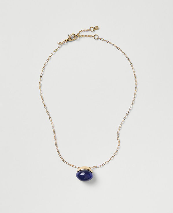 A gold chain necklace with a blue oval pendant rests on a plain light gray background.