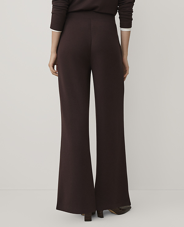 A person stands facing away from the camera wearing dark brown wide-leg trousers and a matching top against a plain, light-colored background.