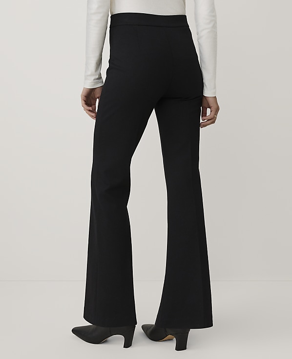 A person wearing a white long-sleeved top, black flared trousers, and black heels stands against a plain light gray background.