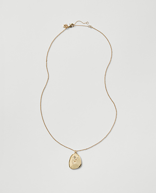 A gold chain necklace with an oval pendant rests against a plain light gray background.