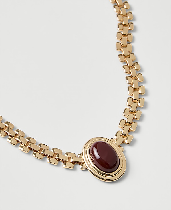 A gold chain necklace with a red oval gemstone pendant rests on a plain white background.