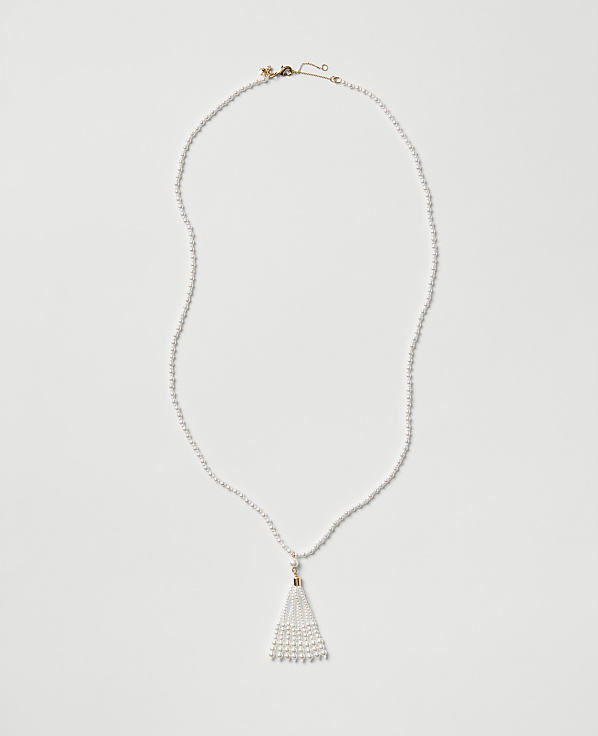 A white pearl necklace with a tassel pendant rests on a plain light gray background.