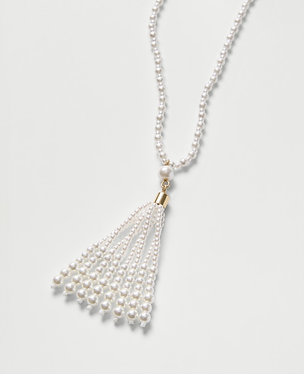 A white pearl necklace with a tassel pendant rests on a plain white background.