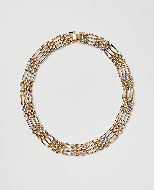 A gold chain necklace is arranged in a circle against a plain light gray background.