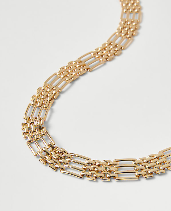 A gold-toned link chain curves across a plain, light gray background.