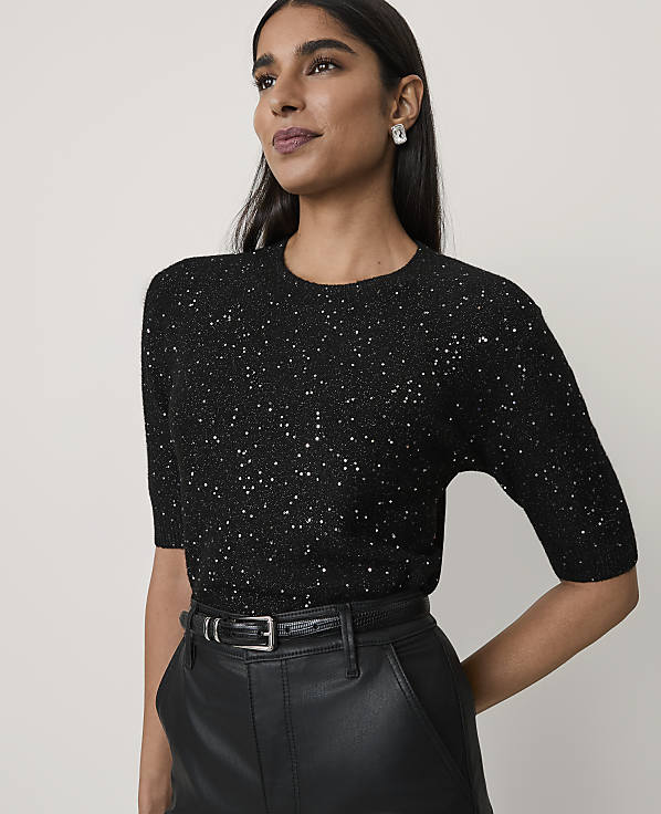 A woman wearing a sparkling black top and leather trousers stands against a plain, light-colored background.