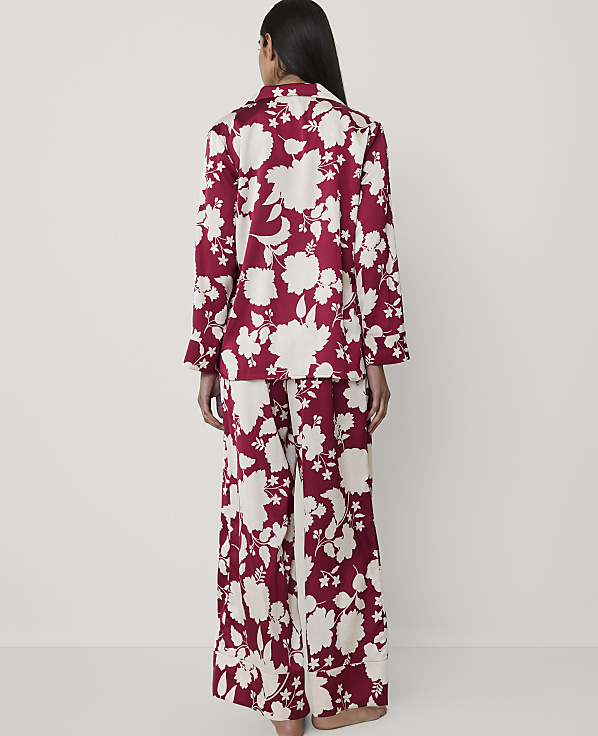 A woman stands with her back to the camera wearing red and white floral pajamas against a plain, light-colored background.
