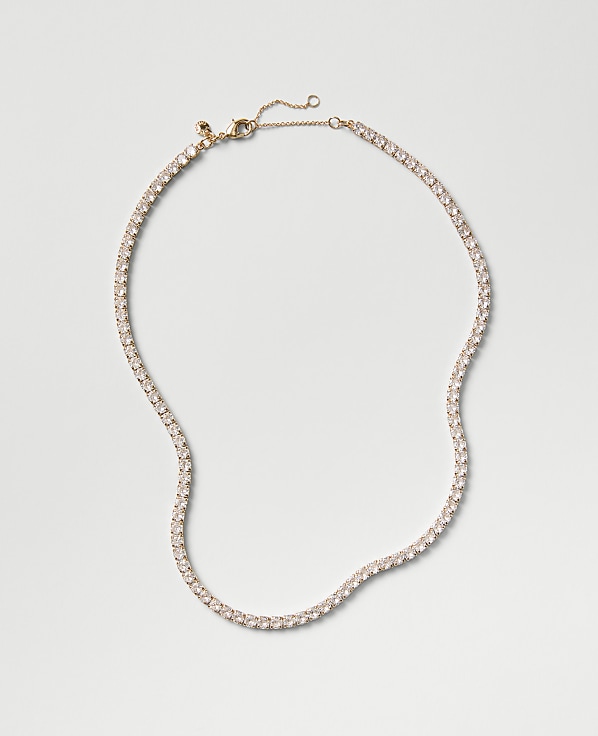 A sparkling tennis necklace with clear stones rests on a plain, light gray background.