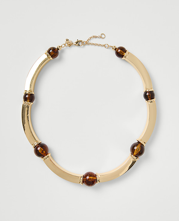A gold-toned necklace with amber-colored beads rests on a plain light gray background.