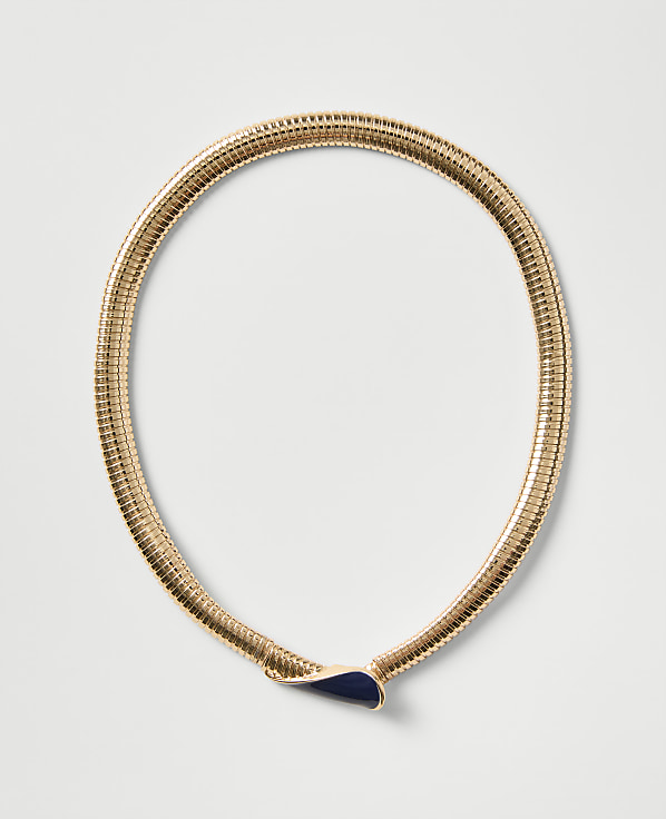 A gold ribbed necklace with a dark blue teardrop-shaped pendant rests on a plain light gray background.