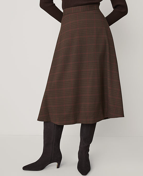 A person wears a brown plaid midi skirt and dark boots against a plain white background.