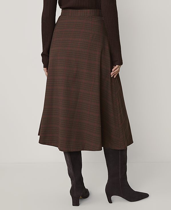 A person wears a brown ribbed top, a brown plaid A-line skirt, and dark brown boots against a plain light gray background.
