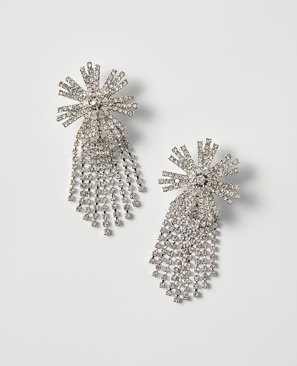 Two sparkling diamond starburst earrings with cascading fringes rest on a plain, light gray background.