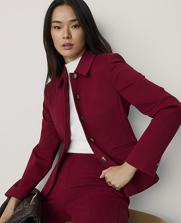 A woman wearing a red blazer and matching trousers over a white top poses against a plain white background.