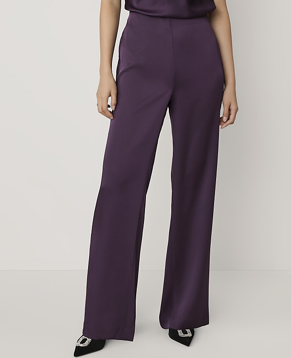 A person wearing purple wide-leg trousers and black pointed heels stands against a plain white background.