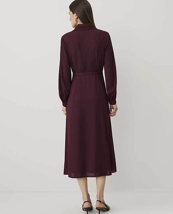 A woman stands with her back to the camera wearing a long-sleeved burgundy dress against a plain white background.