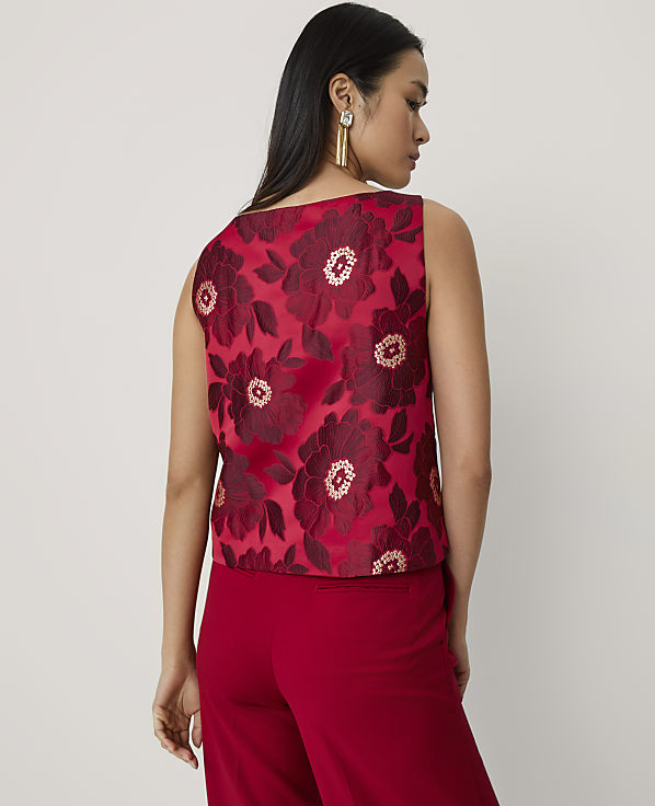 A woman wearing a red floral sleeveless top and matching red trousers stands against a plain, light-colored background.