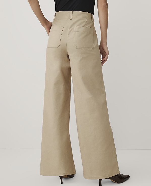 A person wearing a black top and wide-leg khaki trousers stands against a plain white background.