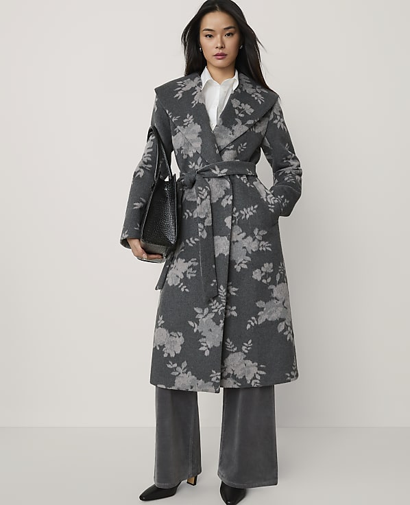A woman wearing a grey floral-patterned wrap coat and wide-leg trousers stands against a plain white background.