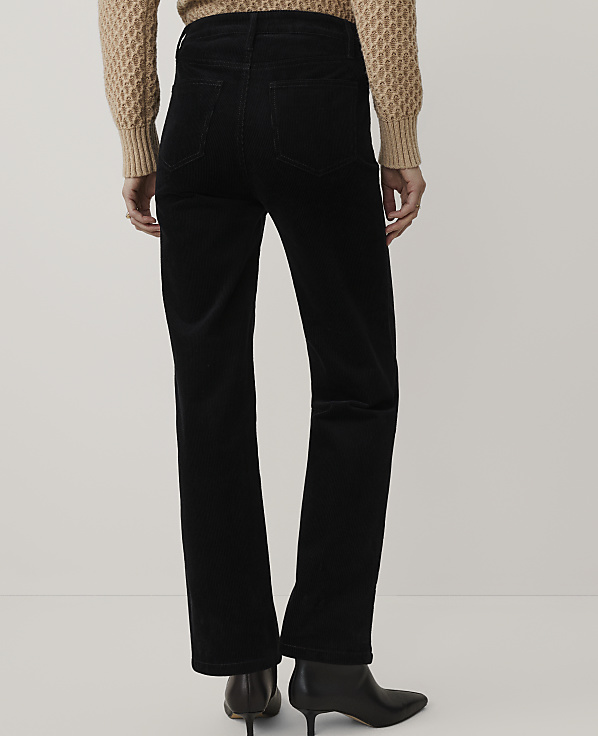 A person wearing a tan knit sweater, black corduroy pants, and black pointed-toe heels stands against a plain white background.