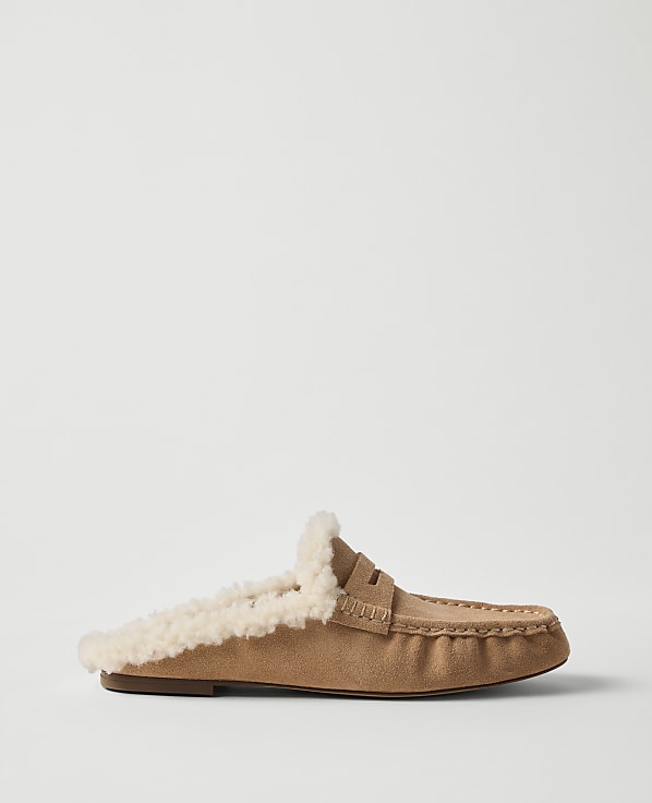 A tan suede slipper with a fluffy white faux-fur lining sits against a plain, light gray background.