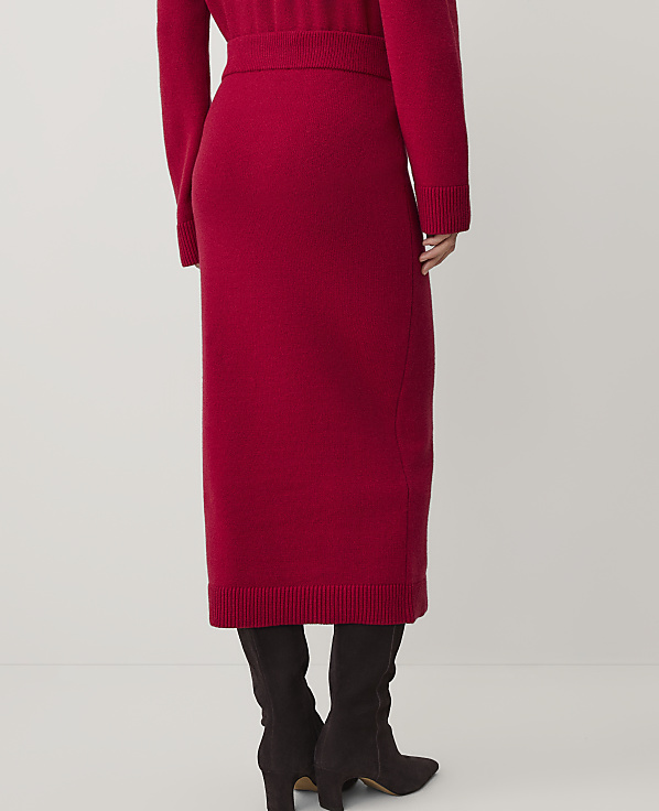 A person wearing a red knit skirt and matching top with dark brown boots stands against a plain white background.