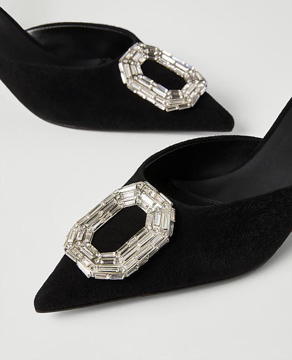 Two black suede pointed-toe heels with large crystal buckles rest on a plain white background.