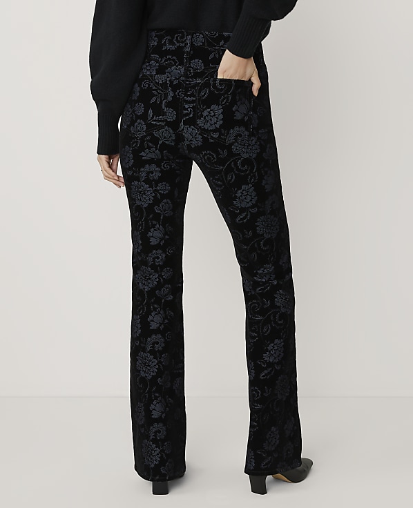 A person wears black floral patterned trousers and a dark sweater against a plain white background.