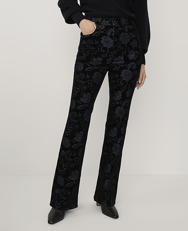 A person wearing a black sweater and floral-patterned black velvet trousers stands against a plain white background.