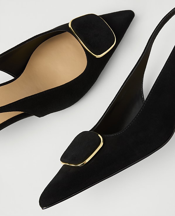 Two black suede pointed-toe slingback heels with gold-trimmed buckles are positioned diagonally against a plain white background.