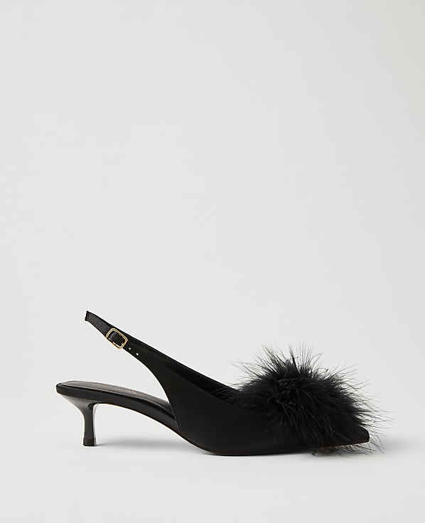 A black satin slingback heel with a fluffy feather pompom on the toe sits against a plain light gray background.