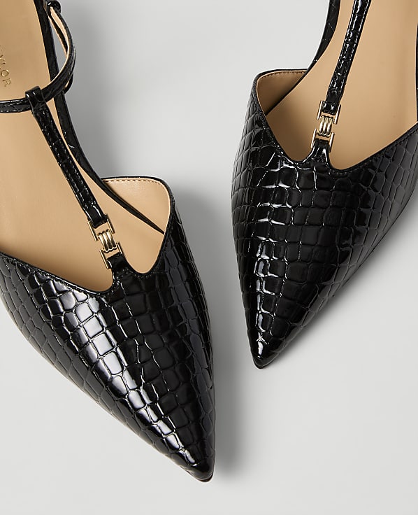 Two black crocodile-embossed pointed-toe flats with gold accents are positioned against a plain light gray background.
