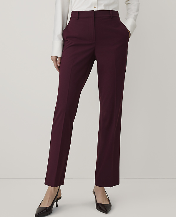 A person wearing a white button-down shirt, burgundy trousers, and black pointed heels stands against a plain white background.