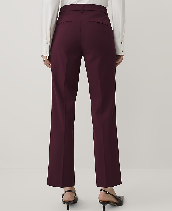 A person wearing a white shirt and burgundy trousers stands against a plain light gray background.