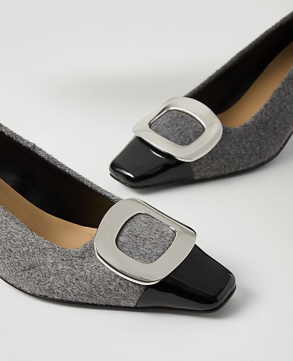 A pair of grey felt pumps with black patent leather toes and silver buckles rest on a plain white surface.