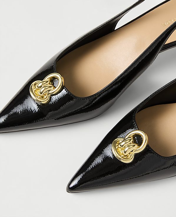 Two black patent leather pointed-toe flats with gold chain ornaments rest on a plain white background.