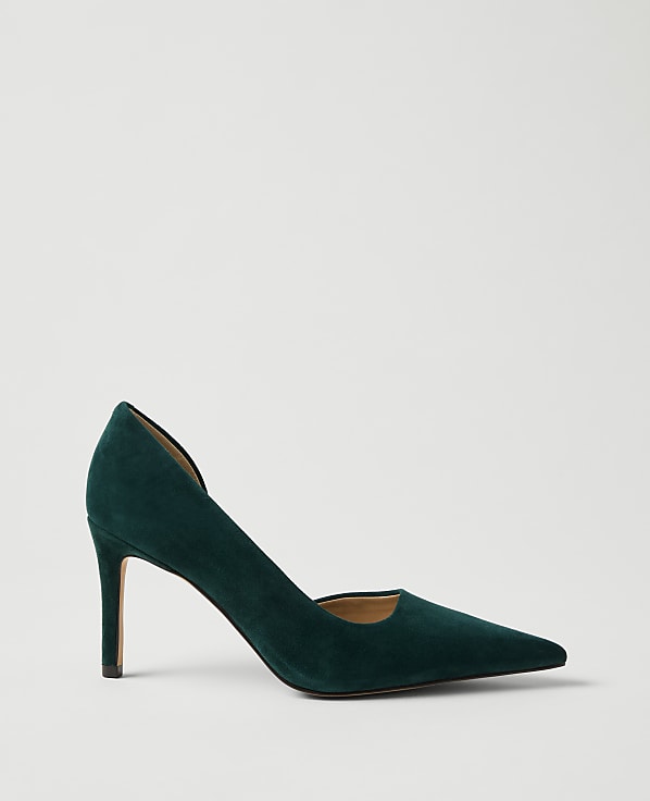 A single dark green suede pointed-toe pump stands against a plain, light gray background.
